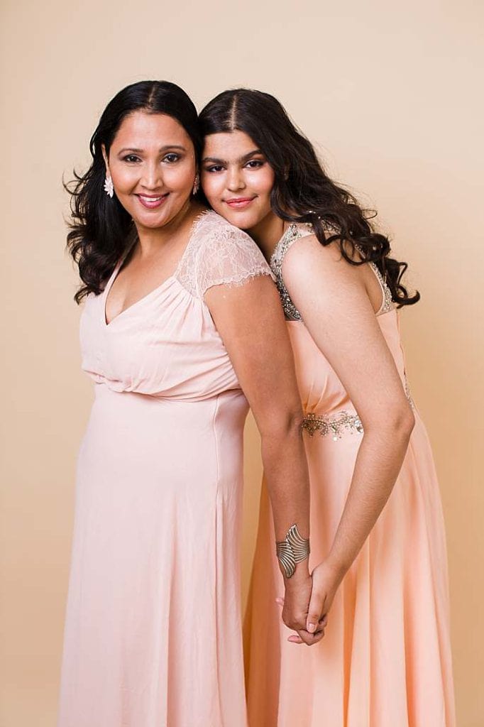 Elegant mother and daughter portrait in matching peach evening gowns, holding hands during a London studio photoshoot.