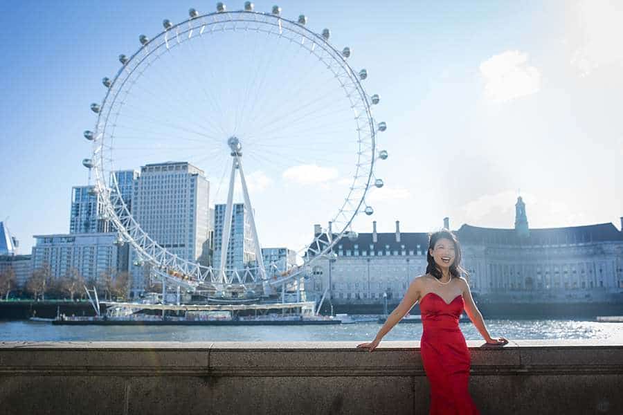 Woman in a red dress smiling in front of the London Eye and River Thames, a prime London photoshoot location